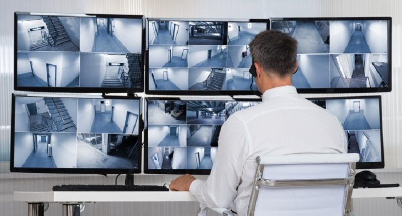 Rear view of security system operator looking at CCTV footage at desk in office